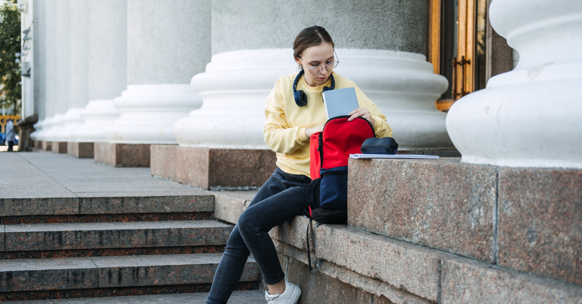 A young woman sitting on college steps looking through her backpack