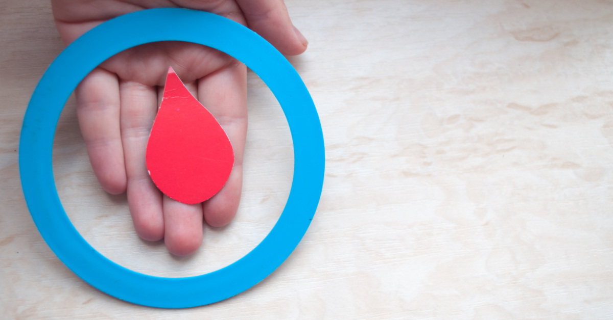 Hand holding paper cutouts of blood drop inside blue circle, representing Diabetes Awareness Month