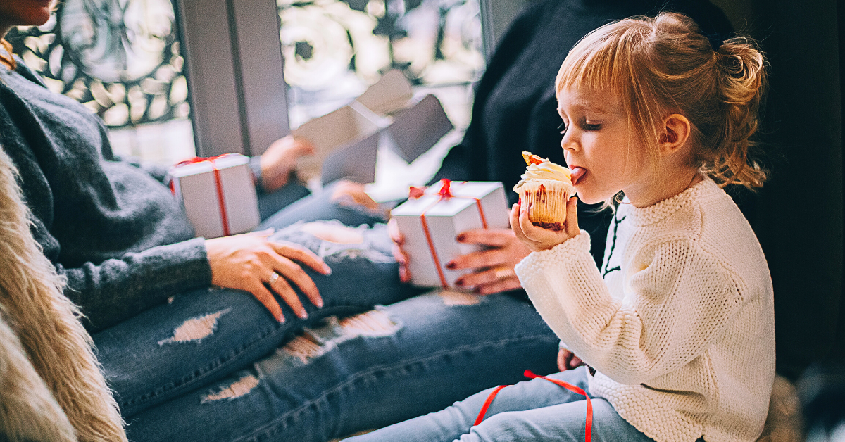 Child sitting next to family while licking frosting off of a cupcake