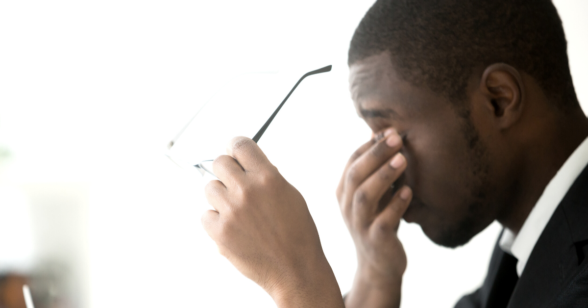 Tired man holding glasses while rubbing his eyes.