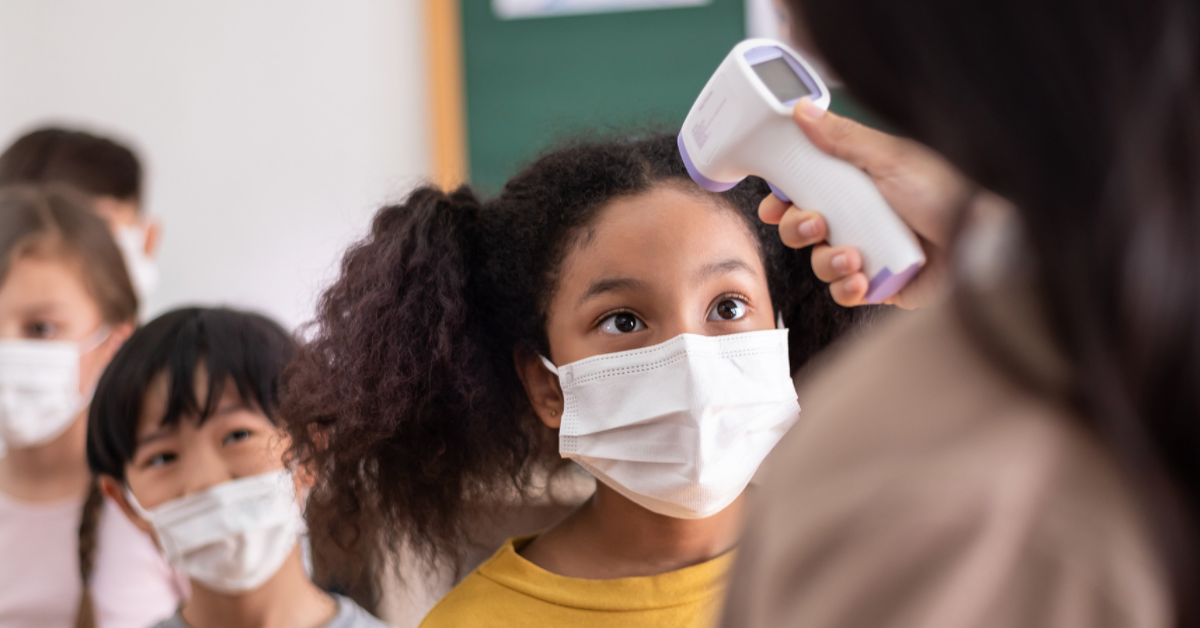 Teacher using no-touch thermometer to check a student's forehead temperature
