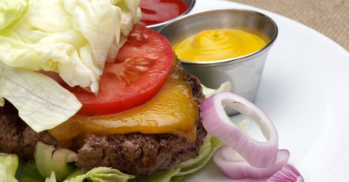 Hamburger wrapped in lettuce with onions, mustard and ketchup on the side